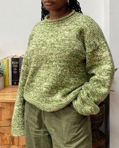 a woman standing in front of a table with books on it and wearing a green sweater