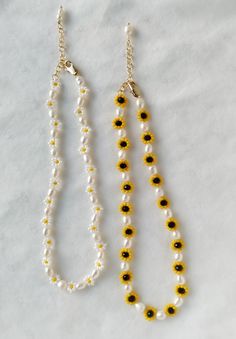 two yellow and white beaded necklaces on a marble surface, one with black beads