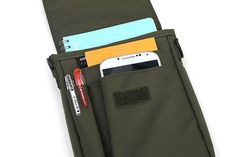 a cell phone is sticking out of the pocket of a green bag with two credit cards and a pen in it