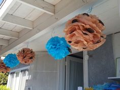 some paper flowers hanging from the side of a house with blue and orange pom poms