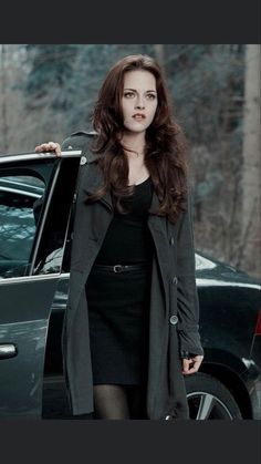 a woman standing next to a car in front of a forest with trees and snow