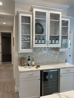 a kitchen with white cabinets and marble counter tops, wine bottles on the cabinet doors