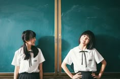 two girls standing in front of a blackboard with their hands on their hipss