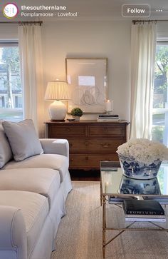 a living room filled with furniture and flowers on top of a coffee table in front of two windows