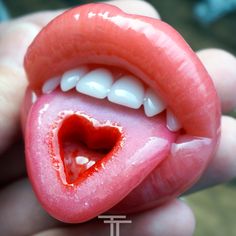 a close up of a person holding a fake tongue with a heart shaped hole in it