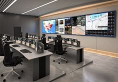 an office with multiple monitors and desks in front of the wall displaying maps on it