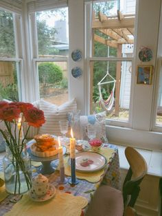 a table with plates and candles on it in front of two windows that look out onto the yard