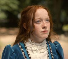 a woman with red hair wearing a blue dress and white collared shirt is looking at the camera