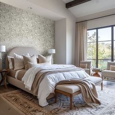 a bedroom with a large bed and two chairs in front of a window that overlooks the trees outside