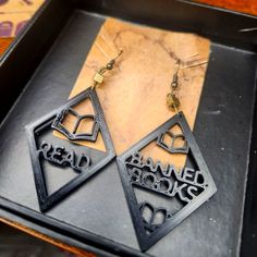 two black earrings with the words read banned books written on them, sitting in a tray