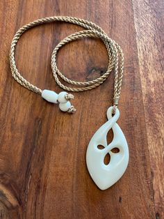 a white necklace on a wooden table with a rope around it and an object in the shape of a leaf