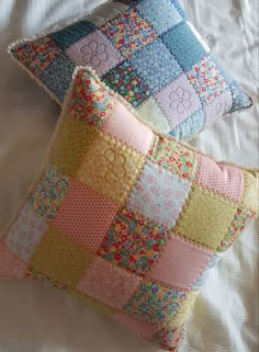 two decorative pillows on a bed with white sheets and pillowcases, one is made out of patchwork