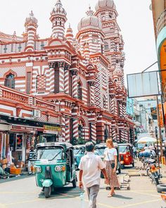 two people walking down the street in front of an old building with many spires