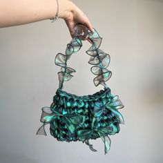 a hand holding a purse made out of green and blue material with ribbons on it