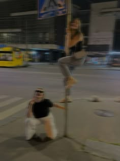 a woman standing on top of a pole next to a man in white shorts and black shirt