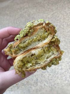 a person holding up a sandwich with pesto and bread crumbs on it