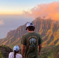 a man and woman standing on top of a mountain looking out at the ocean below