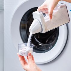 someone is pouring something into a glass in front of a washing machine