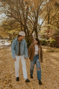 a man and woman walking through leaves in the park with one holding his hand while the other is looking at him