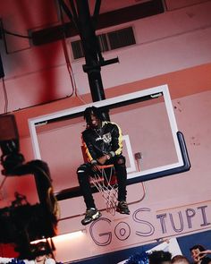 a man sitting on top of a basketball hoop in front of a camera set up