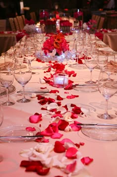 a long table is set with wine glasses and rose petals on the table for a wedding reception