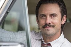 a man with a moustache sitting in a car and smiling at the camera