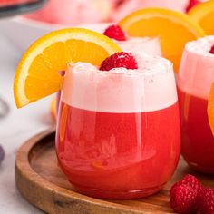 two glasses filled with drinks and garnished with raspberries on a wooden tray