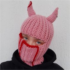 a young boy wearing a knitted pink devil mask with horns on it's head