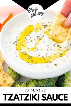 a hand dipping some tortilla chips into a white bowl filled with tzatziki sauce