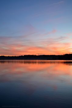 the sun is setting over water with trees in the background