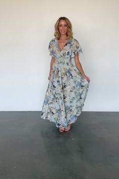 a woman standing in front of a white wall wearing a blue and yellow floral dress