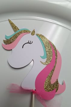 a pink and gold unicorn cake topper on a white plate with a pink bow