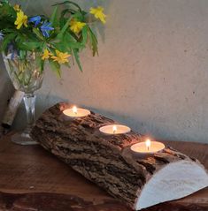 three lit candles sit on a piece of wood next to a vase with yellow flowers