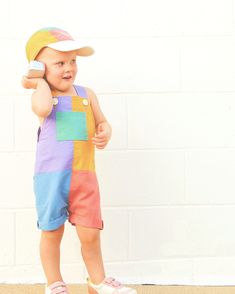 a small child wearing a hat and holding a cell phone to his ear while standing in front of a white brick wall