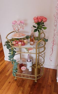 a gold bar cart with pink roses and cupcakes on it, next to some condiments