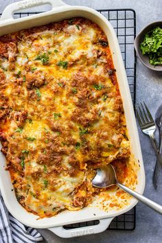 a casserole dish with meat and cheese in it on a cooling rack next to two silver spoons