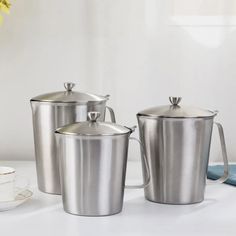 three stainless steel canisters sitting on a white table with yellow flowers in the background