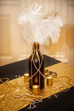 a table topped with a bottle filled with pearls and feathers on top of a table