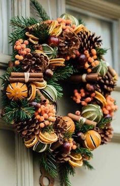 a wreath with pine cones and oranges hanging on a doorknob, decorated with cinnamon sticks