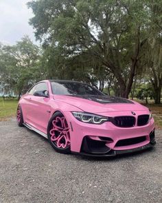 a pink car is parked in front of some trees and grass with bright pink rims