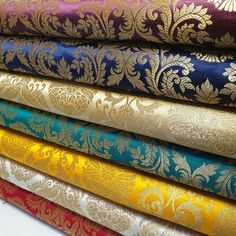 a stack of different colored fabrics with gold, blue and red designs on it's sides