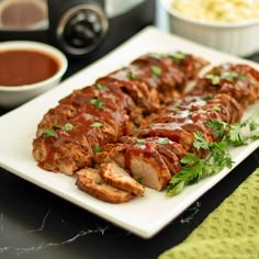 meatloaf with sauce and garnish on a plate next to bowls of dipping sauce