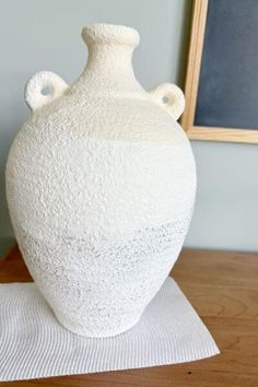 a large white vase sitting on top of a wooden table next to a chalkboard