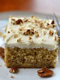 a piece of cake with white frosting and pecans on top sitting on a plate