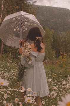 a woman holding an umbrella standing in a field of daisies and wildflowers