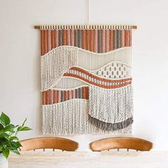 two wooden chairs sitting in front of a wall hanging