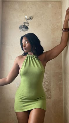 a woman in a short green dress standing next to a shower head and hand on the wall