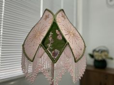 a pink and green chandelier hanging from the ceiling in a room with blinds