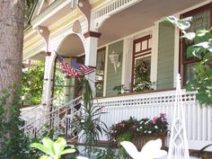 an american flag on the porch of a house with potted plants and flowers in front