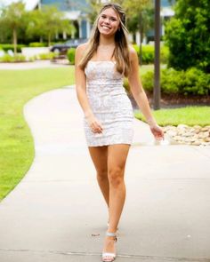 a woman in a white dress is walking down the sidewalk with her hand on her hip